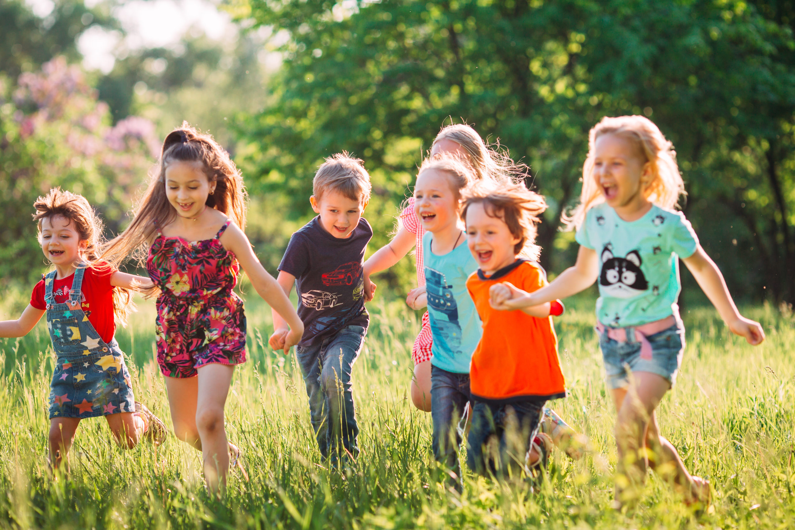 Large group of kids, friends boys and girls running in the park on sunny summer day in casual clothes
